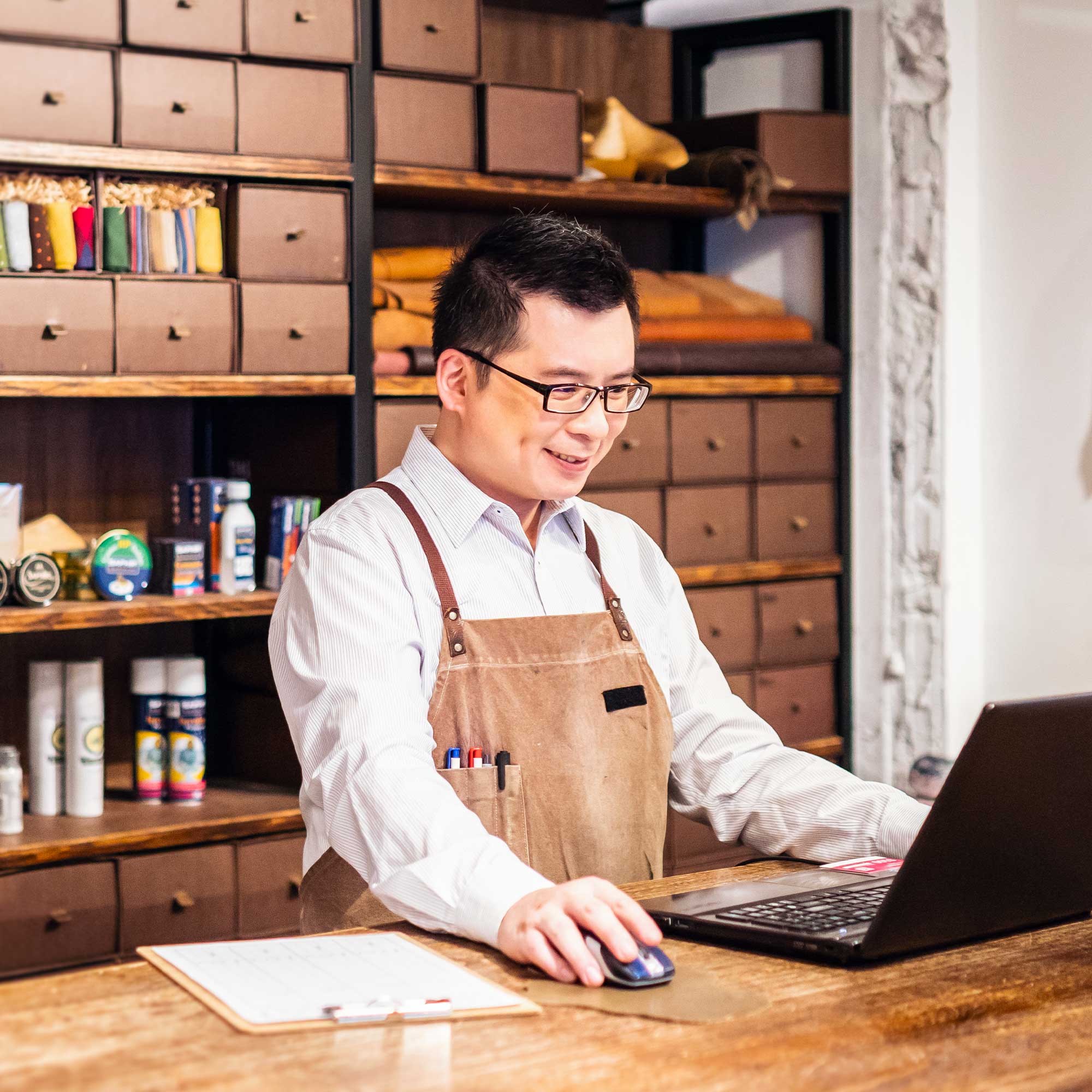A man stands at his computer wearing a white button up shirt and apron.
